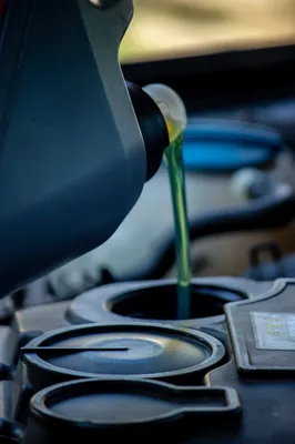 Acercamiento de un bote de aceite siendo vaciado en el depósito del motor como parte del mantenimiento y de la explicación de cómo checar el aceite de transmisión automática para rellenarlo cuando sea necesario