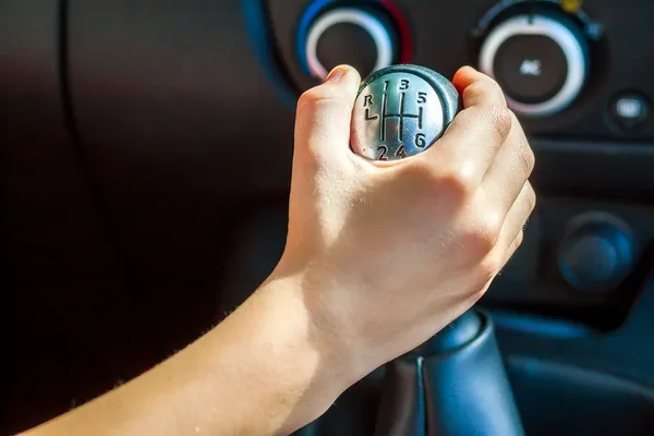 Primer plano de una mano agarrando una palanca de cambios manual con el patrón R-1-3-5 y 2-4-6 de la caja de velocidades estándar.