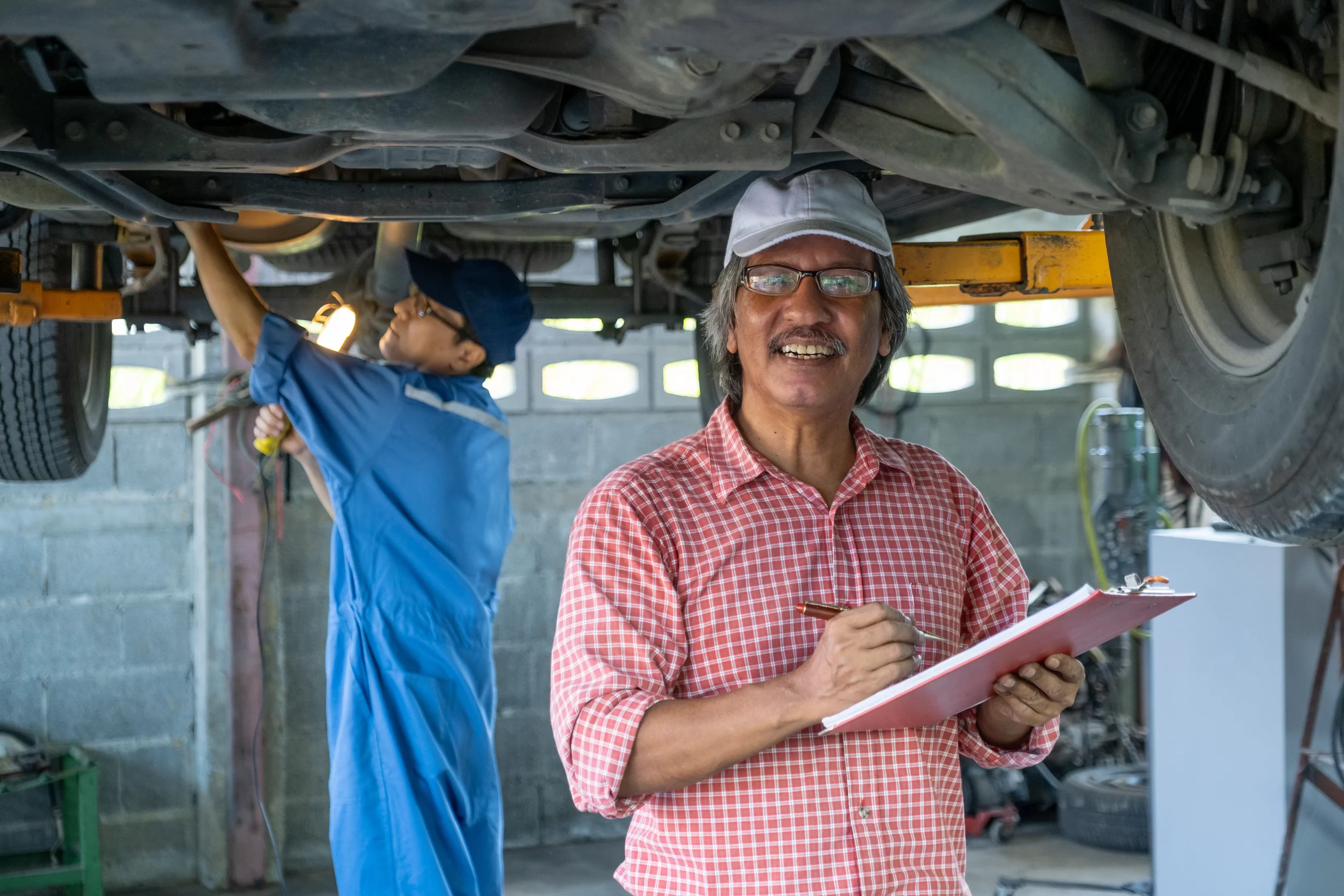 Gerente supervisa a mecánico que trabaja en los bajos de un vehículo, verificando el sistema de transmisión estándar