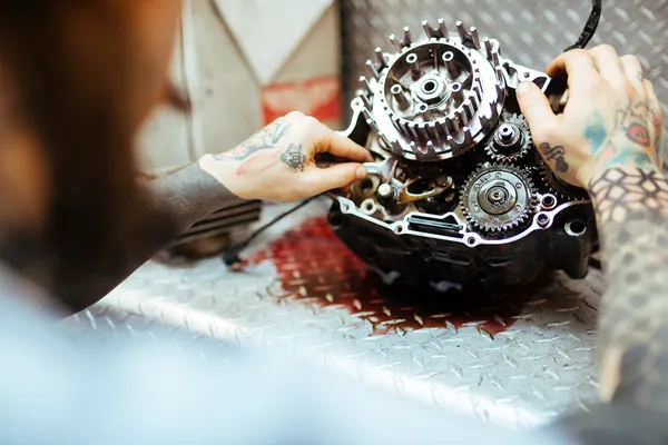 Transmisión semiabierta sobre un soporte en el taller, mostrando la cadena y piñones. Son esenciales refacciones de transmisiones automáticas o manuales.