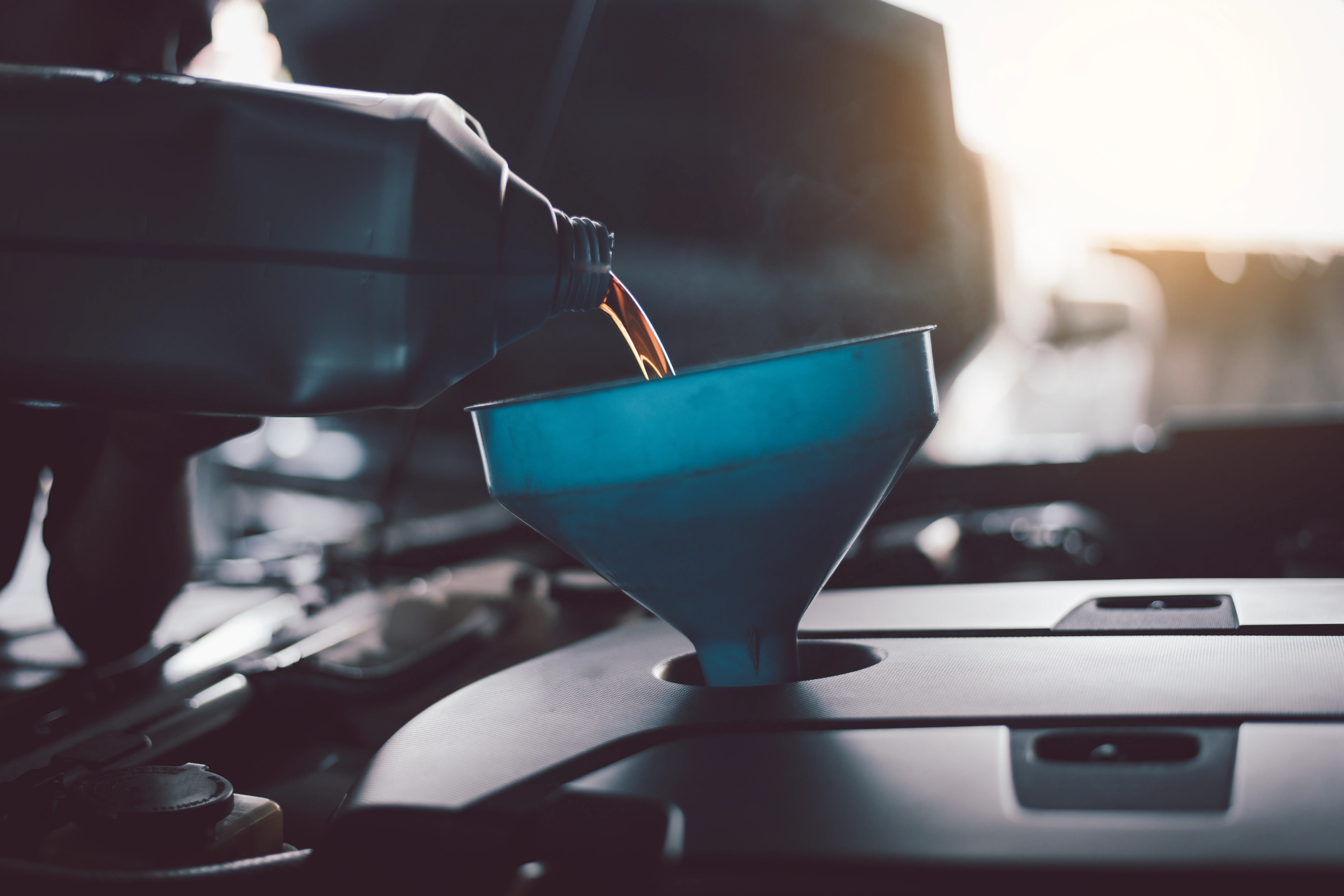 Mecánico vertiendo aceite nuevo a través de un embudo azul en un motor moderno con vapor visible por el calor.