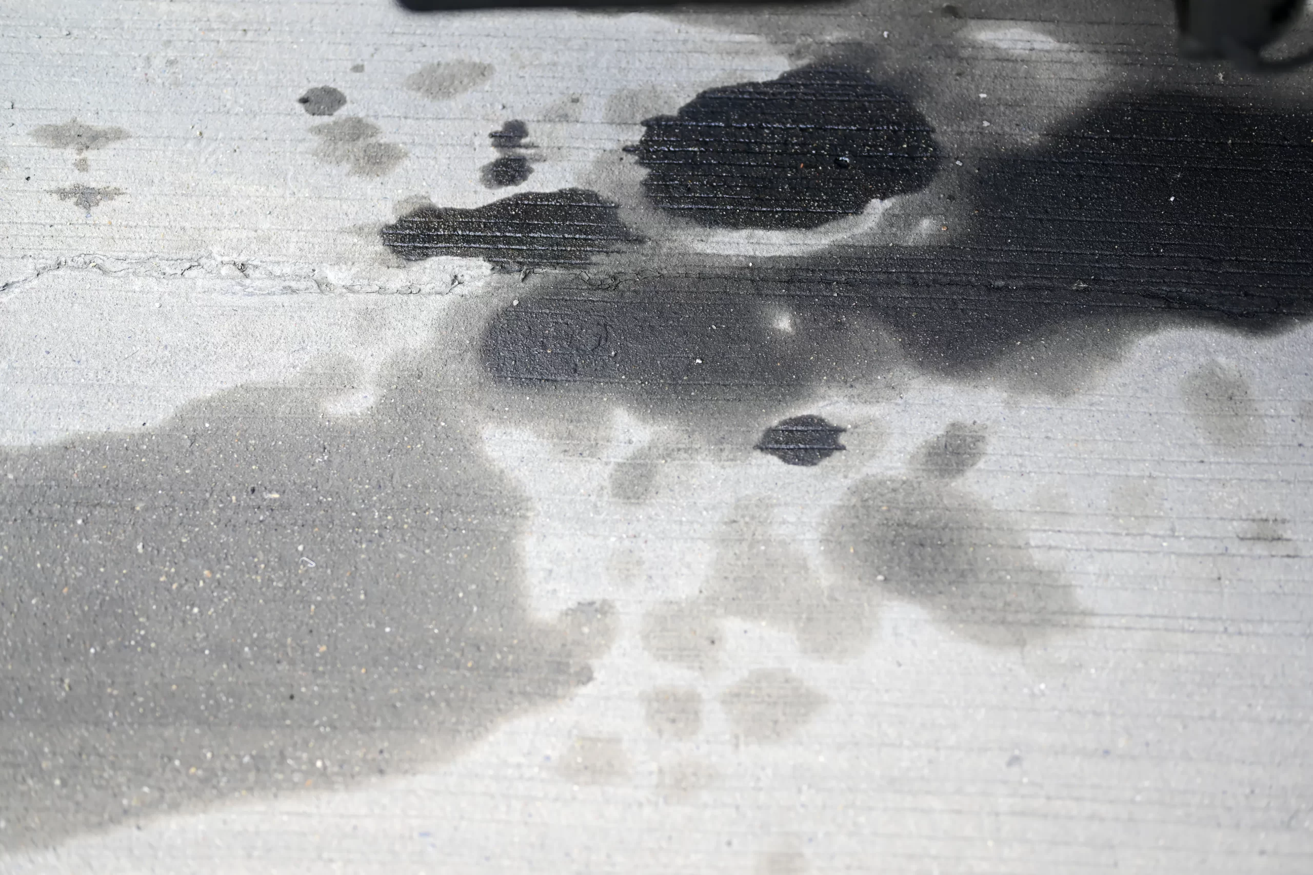 Mancha de aceite en el suelo bajo un auto; recuerda que es peligroso manejar con la transmisión fallando por fugas.
