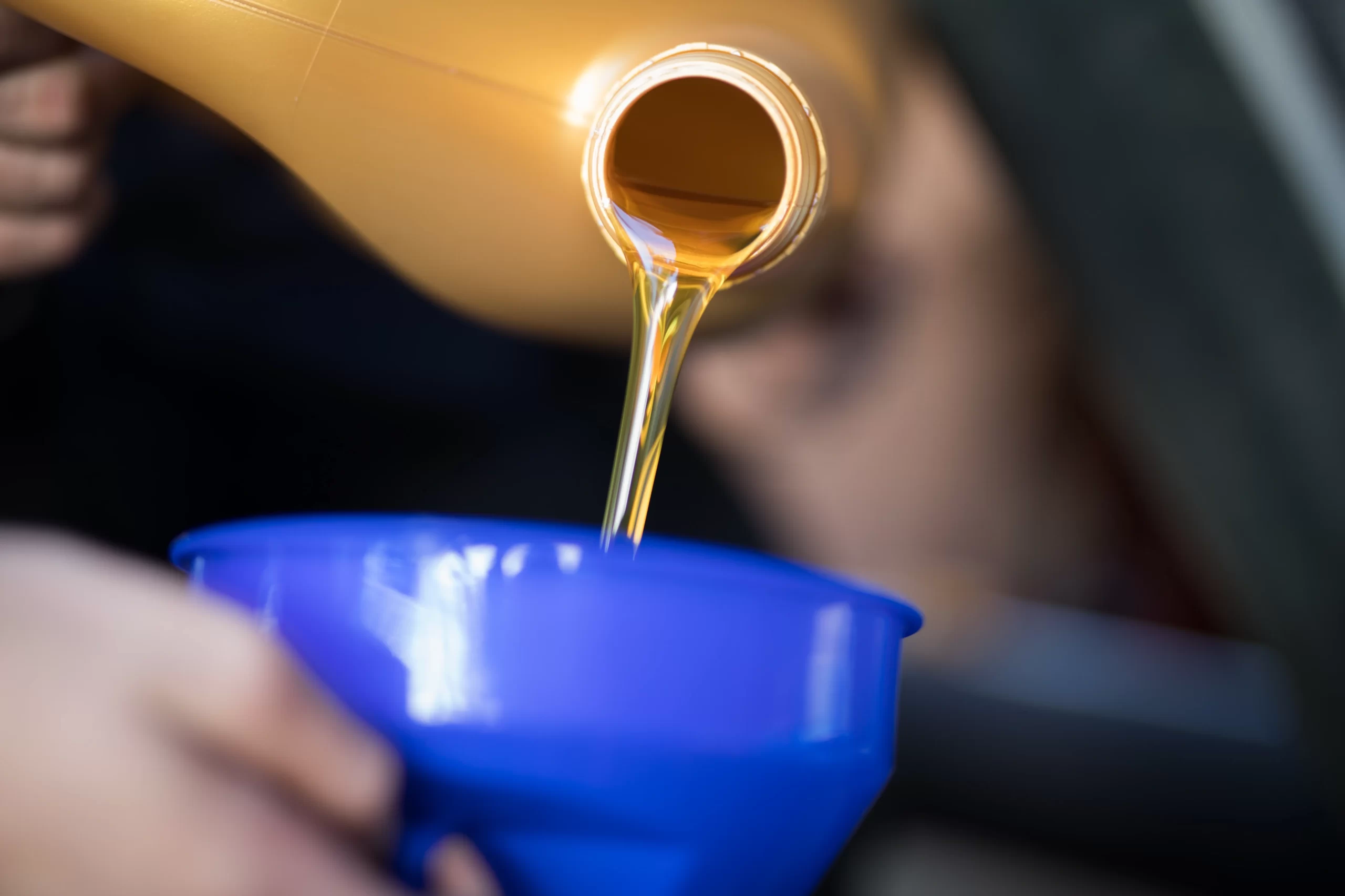 Persona vertiendo lubricantes automotrices dorados desde una botella hacia un embudo azul para el motor del carro.