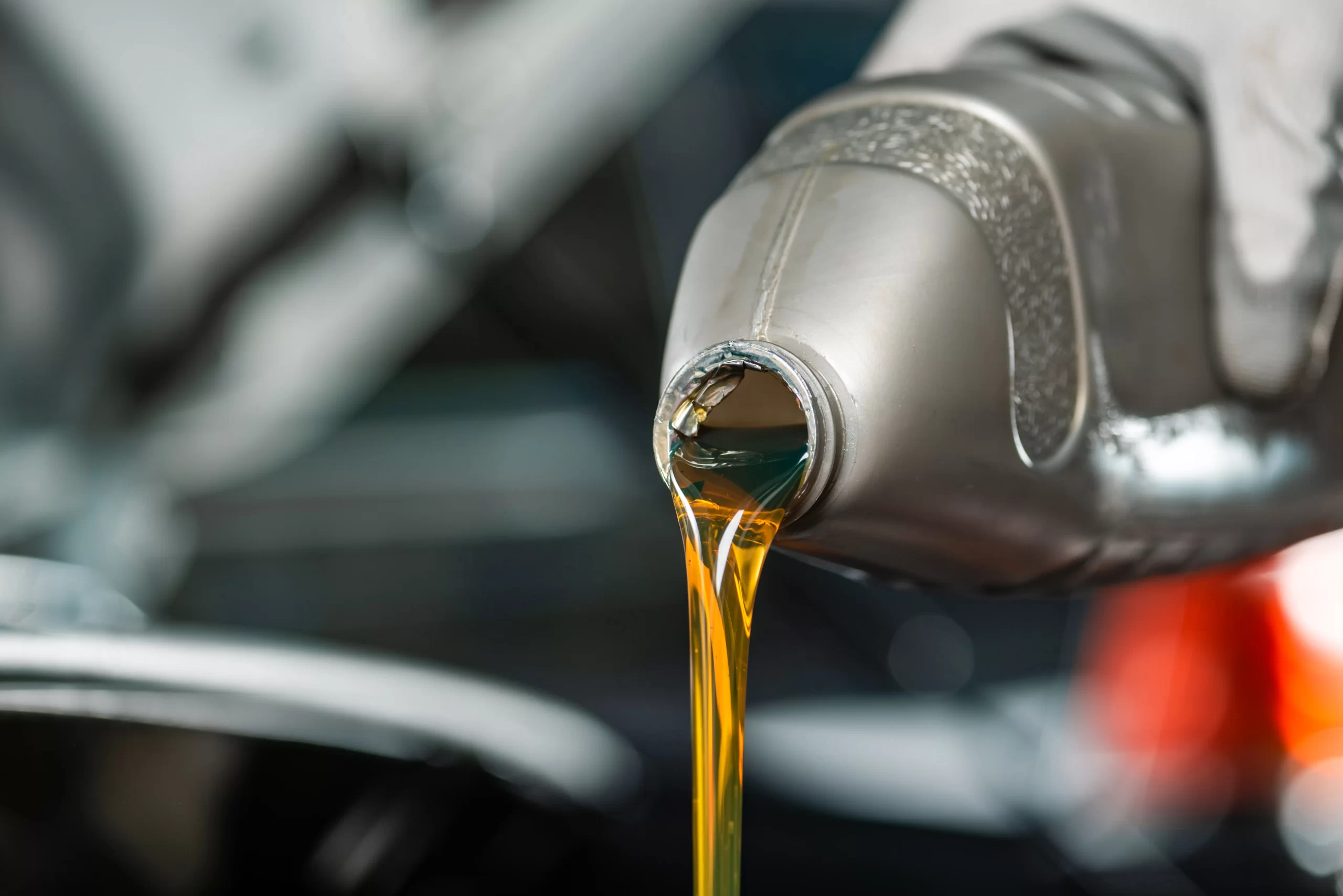 Vertido de lubricantes automotrices dorados y fluidos desde una botella gris de plástico en un taller.